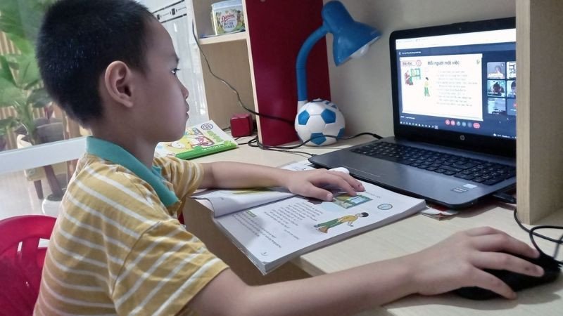 Hình ảnh một bạn trẻ đang dùng điện thoại thông minh với hình nền một bàn học đầy sách, gợi ý việc sử dụng thiết bị để hỗ trợ học tập