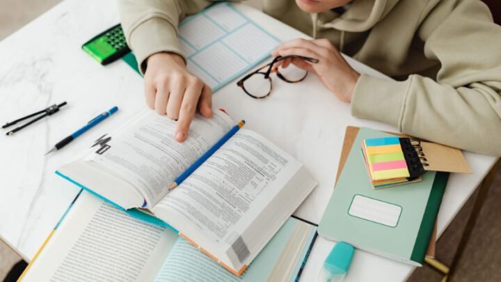 Một người phụ nữ trẻ đang học bài tại bàn làm việc với sách và bút, thể hiện sự chăm chỉ và tập trung