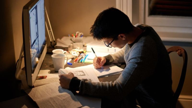 Một sinh viên đang ngồi học tập chăm chú, có lẽ đang đọc sách hoặc ghi chú, thể hiện tinh thần cầu tiến và nỗ lực