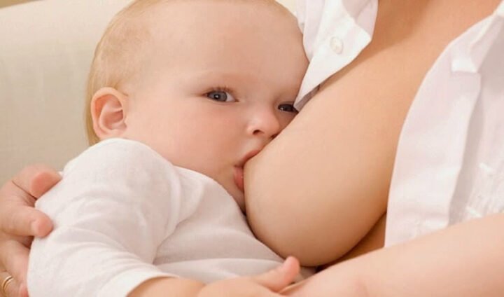 Người phụ nữ đang ôm và cho em bé bú sữa mẹ, biểu tượng của sự chăm sóc và nuôi dưỡng