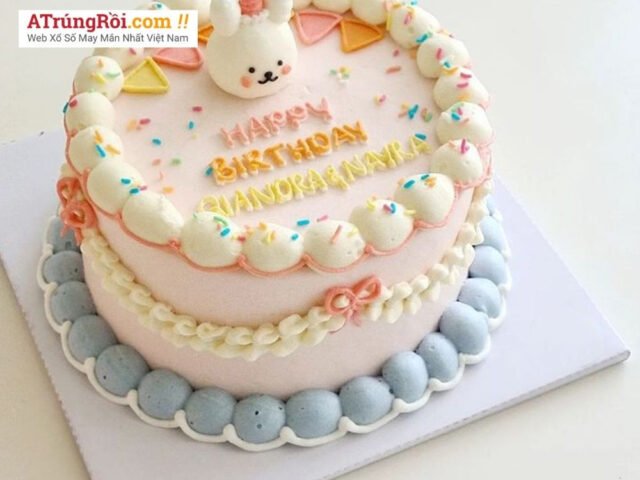 Một chiếc bánh kem sinh nhật nhiều màu sắc đang được một bàn tay đặt trên bàn ăn