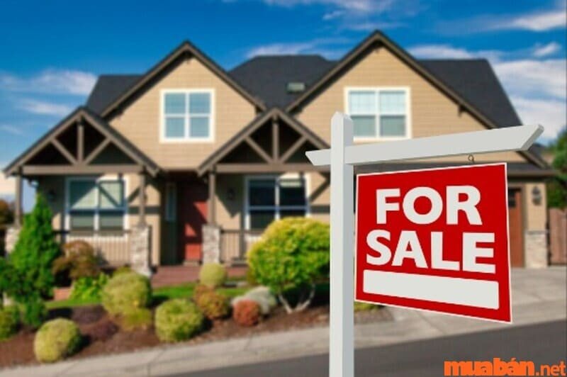 Người phụ nữ đang đứng trước bảng hiệu "For Sale" của ngôi nhà mình, thể hiện sự chủ động trong việc rao bán