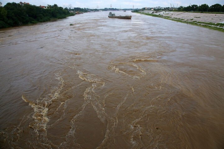 Người phụ nữ đứng bên bờ sông ngắm dòng nước chảy xiết, biểu trưng cho cảm xúc và dòng chảy cuộc sống trong giấc mơ